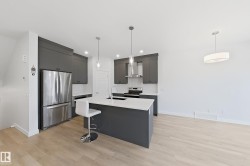 Modern kitchen featuring dark cabinetry, stainless steel appliances, a white subway tile backsplash, and light wood-finish flooring - 