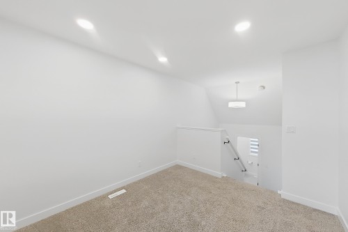 Carpeted floor area featuring recessed lighting, a vaulted ceiling, and a modern drum pendant light fixture illuminating the stairwell - 7791 Eifert Crescent Nw, Edmonton, AB - Indoor Photo Showing Other Room