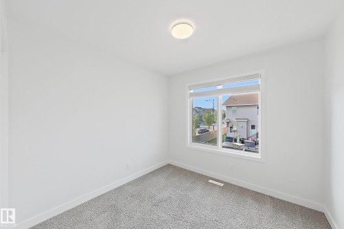 Room featuring a large window with white trim, neutral carpet flooring, a flush-mount ceiling light fixture, and white painted walls - 7791 Eifert Crescent Nw, Edmonton, AB - Indoor Photo Showing Other Room