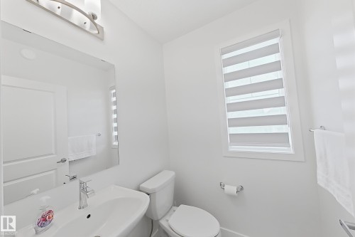 Modern powder room featuring a white pedestal sink with chrome faucet, toilet, and a window with horizontal blinds - 7791 Eifert Crescent Nw, Edmonton, AB - Indoor Photo Showing Bathroom