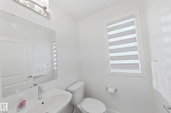 Modern powder room featuring a white pedestal sink with chrome faucet, toilet, and a window with horizontal blinds - 