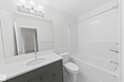Modern bathroom featuring a single vanity with a white countertop, undermount sink, and dark gray cabinetry - 