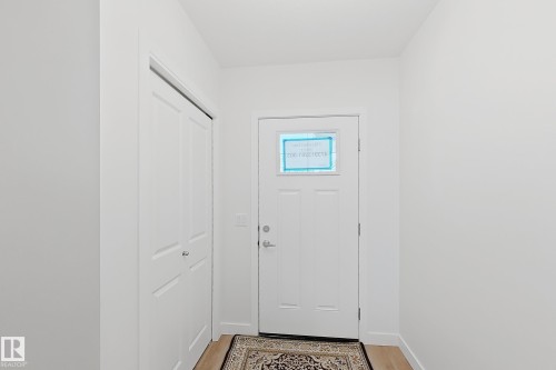 Entryway featuring a paneled door with glass insert, light wood-finish flooring, and a white bi-fold closet door - 7791 Eifert Crescent Nw, Edmonton, AB - Indoor Photo Showing Other Room