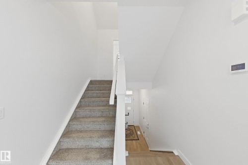Carpeted staircase with white balusters, leading to a foyer featuring wood-finish flooring and a white entry door with glass inserts - 7791 Eifert Crescent Nw, Edmonton, AB - Indoor Photo Showing Other Room