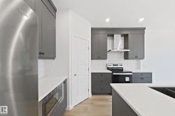 Modern kitchen featuring sleek gray cabinetry, stainless steel appliances, white countertops, and a white subway tile backsplash - 