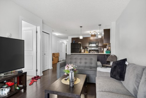 Open-concept living space featuring wood-finish flooring, white walls, and a kitchen with dark cabinetry and stainless steel appliances - 3353 16A Avenue Nw, Edmonton, AB - Indoor Photo Showing Living Room