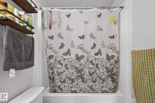 Fiberglass tub with a white shower surround, accompanied by wall-mounted shelving and a towel bar - 3353 16A Avenue Nw, Edmonton, AB - Indoor Photo Showing Bathroom