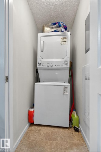 Dedicated laundry alcove featuring a stacked washer and dryer unit, and vinyl flooring - 3353 16A Avenue Nw, Edmonton, AB - Indoor Photo Showing Laundry Room