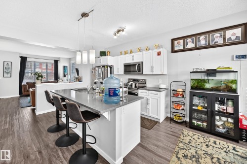 Kitchen island with gray countertop, white shaker cabinetry, stainless steel appliances, and wood-finish flooring - 1929 24 Street Nw, Edmonton, AB - Indoor Photo Showing Kitchen With Upgraded Kitchen