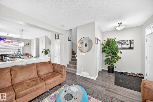 Open-concept living area featuring warm wood-finish flooring, a caramel-toned upholstered sofa, and abundant natural light from multiple windows - 1929 24 Street Nw, Edmonton, AB - Indoor Photo Showing Living Room