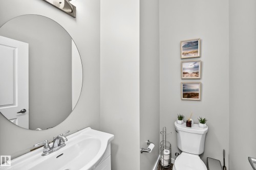 White pedestal sink with chrome faucet, circular mirror, and wall-mounted vanity lighting - 1929 24 Street Nw, Edmonton, AB - Indoor Photo Showing Bathroom