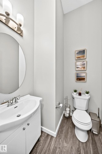 Wood-finish flooring, white vanity with integrated sink, circular mirror, and wall-mounted vanity lighting - 1929 24 Street Nw, Edmonton, AB - Indoor Photo Showing Bathroom