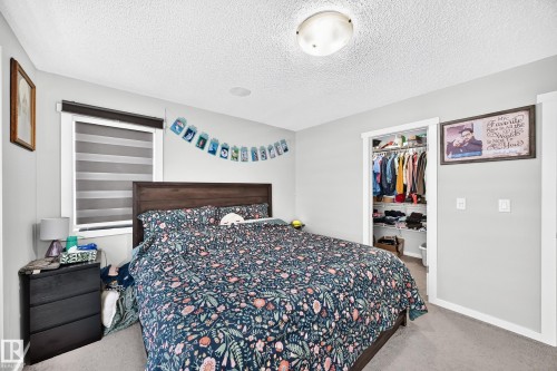 Light gray wall paint, dark wood-finish headboard, window with horizontal blinds, built-in open closet with shelving, and overhead flush mount lighting - 1929 24 Street Nw, Edmonton, AB - Indoor Photo Showing Bedroom