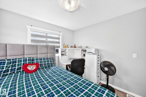 Bright secondary bedroom featuring a cushioned upholstered headboard, geometric patterned bedding, built-in desk workspace with white cabinetry and shelving, and a ceiling-mounted light fixture - 1929 24 Street Nw, Edmonton, AB - Indoor