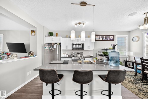 Kitchen featuring a central island with countertop seating, stainless steel appliances, white cabinetry, and wood-finish flooring - 1929 24 Street Nw, Edmonton, AB - Indoor Photo Showing Kitchen With Upgraded Kitchen