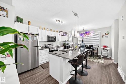 White cabinetry, stainless steel appliances, wood-finish flooring, island with countertop seating, and recessed lighting - 1929 24 Street Nw, Edmonton, AB - Indoor Photo Showing Kitchen With Stainless Steel Kitchen