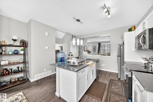 Kitchen featuring a central island with a sink, stainless steel appliances, white cabinetry, and wood-finish flooring - 1929 24 Street Nw, Edmonton, AB - Indoor Photo Showing Kitchen