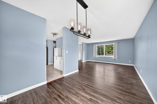Wood-finish flooring throughout, modern chandelier, large window with outdoor scenery, recessed lighting, and white cabinetry - 16808 100 Street Nw, Edmonton, AB - Indoor Photo Showing Other Room