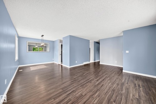 Wood-finish flooring throughout, light blue wall paint, white trim, and a contemporary ceiling light fixture - 16808 100 Street Nw, Edmonton, AB - Indoor Photo Showing Other Room