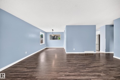 Spacious interior with wood-finish flooring, light blue walls, white trim, and a contemporary ceiling fixture - 16808 100 Street Nw, Edmonton, AB - Indoor Photo Showing Other Room