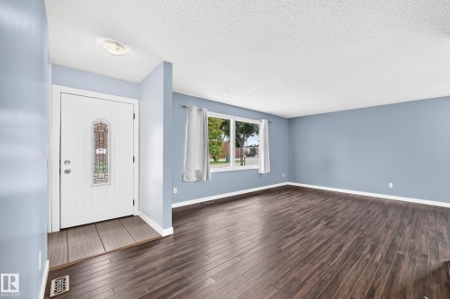 Entryway featuring a decorative glass door and tile flooring, opening to a living area with wood-finish flooring, a large window, and light blue walls - 16808 100 Street Nw, Edmonton, AB - Indoor Photo Showing Other Room