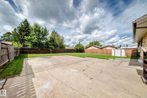 Expansive concrete patio with a manicured lawn, surrounded by a wood fence, mature trees, and a white storage shed - 16808 100 Street Nw, Edmonton, AB - Outdoor
