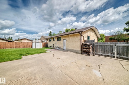 Exterior featuring stucco siding, a shingled roof, a concrete patio, a wooden fence, and a storage shed - 16808 100 Street Nw, Edmonton, AB - Outdoor