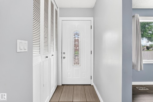Entryway featuring a white door with decorative glass, louvered bi-fold closet doors, light gray walls, and wood-finish tile flooring - 16808 100 Street Nw, Edmonton, AB - Indoor Photo Showing Other Room