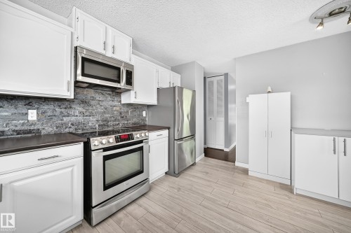 Kitchen featuring white cabinetry, stainless steel appliances, a stone tile backsplash, wood-finish flooring, and track lighting - 16808 100 Street Nw, Edmonton, AB - Indoor Photo Showing Kitchen With Stainless Steel Kitchen