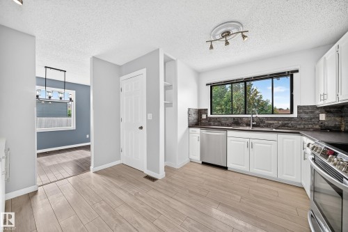 Kitchen featuring white cabinetry, stainless steel appliances, dark countertops, and a stone-finish backsplash - 16808 100 Street Nw, Edmonton, AB - Indoor Photo Showing Kitchen
