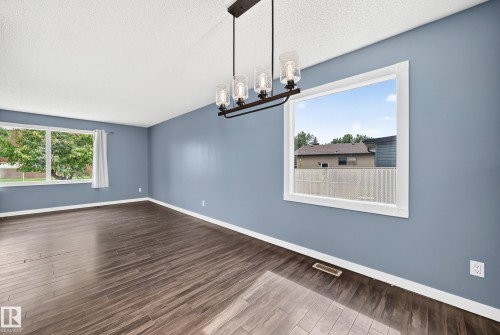 Wood-finish flooring, white window trim, and a linear chandelier with glass shades - 16808 100 Street Nw, Edmonton, AB - Indoor Photo Showing Other Room