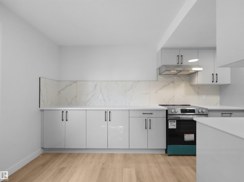 Kitchen featuring wood-finish flooring, white cabinetry, a tile backsplash, and a stainless steel range with an overhead hood - 126 Woodstock Nw, Edmonton, AB - Indoor Photo Showing Kitchen
