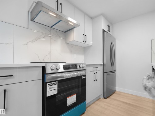 Stainless steel range with sleek vent hood, white upper cabinetry, light wood-finish flooring, and a stone-look backsplash - 126 Woodstock Nw, Edmonton, AB - Indoor Photo Showing Kitchen
