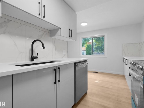 White cabinetry with black hardware, stone-look backsplash, light wood-finish flooring, and a stainless steel dishwasher - 126 Woodstock Nw, Edmonton, AB - Indoor Photo Showing Kitchen