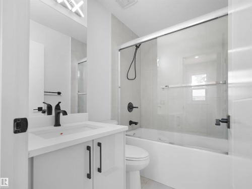 Bathroom featuring a white vanity with integrated sink, matte black fixtures, an illuminated mirror, a toilet, and a bathtub with a clear glass sliding door - 126 Woodstock Nw, Edmonton, AB - Indoor Photo Showing Bathroom