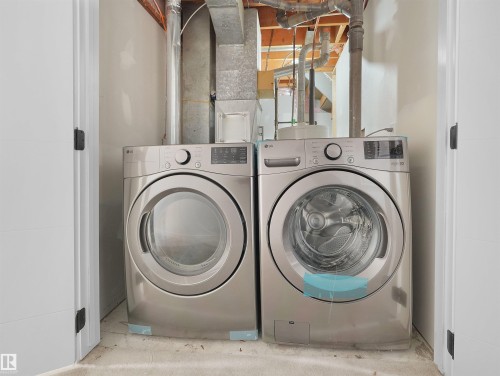 Laundry area featuring a front-loading washer and dryer set, neutral wall paint, and exposed ductwork - 126 Woodstock Nw, Edmonton, AB - Indoor Photo Showing Laundry Room