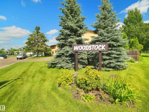 Woodstock sign with landscaped base, surrounded by mature evergreen trees, and expansive green lawn - 126 Woodstock Nw, Edmonton, AB - Outdoor With View