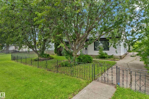 White-sided residence featuring a dark-framed window, mature trees, and a decorative wrought iron fence - 9416 153 Street Nw, Edmonton, AB - Outdoor