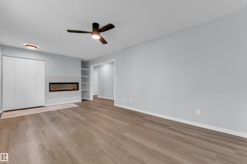 Spacious room featuring wood-finish flooring, a wall-mounted electric fireplace with a tiled surround, and integrated shelving - 9416 153 Street Nw, Edmonton, AB - Indoor With Fireplace