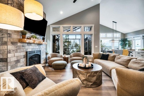 Vaulted ceilings, a stone-faced fireplace with a mantel, large fixed-pane windows with the back drop of Sparkling Pigeon Lake water - 180 Crystal Springs Drive, Rural Wetaskiwin County, AB - Indoor Photo Showing Living Room With Fireplace