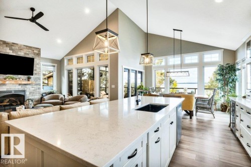 Vaulted ceiling with recessed lighting, stone-clad fireplace, kitchen island with integrated sink, extensive window array, and wood-finish flooring - 180 Crystal Springs Drive, Rural Wetaskiwin County, AB - Indoor Photo Showing Kitchen With Fireplace With Double Sink With Upgraded Kitchen