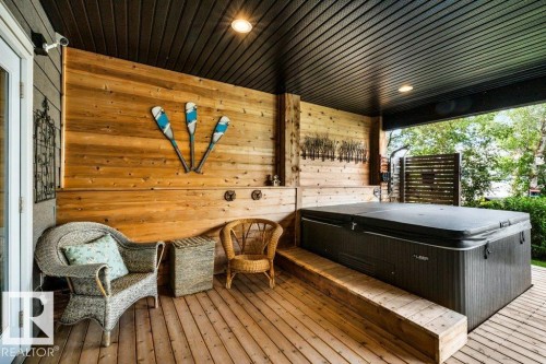 Covered patio featuring a hot tub, wood-finish decking, and slatted wood wall paneling. on the private lake facing lower deck - 180 Crystal Springs Drive, Rural Wetaskiwin County, AB - Outdoor With Deck Patio Veranda With Exterior