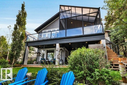 Two-story residence featuring a gray exterior siding, an upper-level glass-paneled balcony, a screened-in porch with a transparent roof, a ground-level covered patio, and exterior wood stairs with a black metal railing - 180 Crystal Springs Drive, Rural Wetaskiwin County, AB - Outdoor