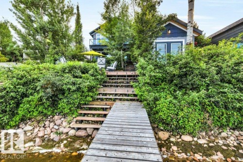 Waterfront property featuring a dock, stone and rock shoreline, staircase, and lush landscaping - 180 Crystal Springs Drive, Rural Wetaskiwin County, AB - Outdoor
