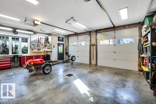 Spacious garage featuring two overhead doors with windows, an additional side door, multiple windows, and extensive built-in workbench cabinetry - 180 Crystal Springs Drive, Rural Wetaskiwin County, AB - Indoor Photo Showing Garage