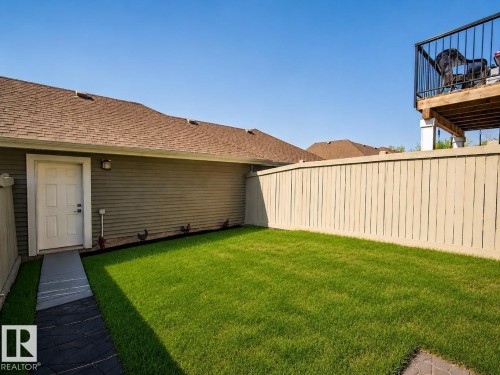 Private backyard featuring a manicured lawn, full privacy fencing, and a paved walkway leading to an exterior entrance - 4013 Blackbird Link Nw, Edmonton, AB - Outdoor With Exterior