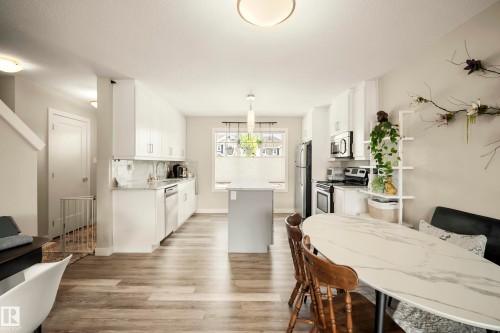 Open-concept kitchen and dining area featuring wood-finish flooring, white cabinetry, a built-in dishwasher, and stainless steel appliances - 4013 Blackbird Link Nw, Edmonton, AB - Indoor Photo Showing Dining Room