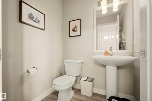 Pedestal sink with a framed mirror and overhead vanity lighting, complemented by wood-finish flooring - 4013 Blackbird Link Nw, Edmonton, AB - Indoor Photo Showing Bathroom