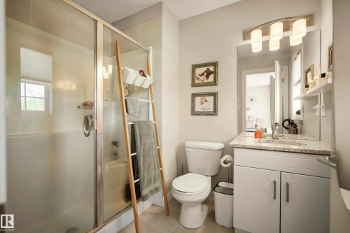 Glass-enclosed shower, single vanity with light-toned countertop, recessed sink, lower cabinetry, and wall-mounted light fixture - 4013 Blackbird Link Nw, Edmonton, AB - Indoor Photo Showing Bathroom