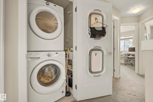 Dedicated laundry closet with stacked washer and dryer, adjacent to a carpeted hallway - 4013 Blackbird Link Nw, Edmonton, AB - Indoor Photo Showing Laundry Room